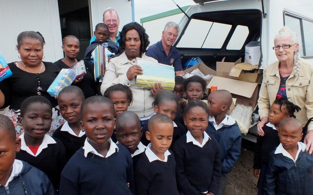Agter vlnr is Jack Doyle, Nonisokolo Mani (skoolhoof), Malcolm Bury en Anita Doyle saam met leerders tydens die oorhandiging van groot hoeveelhede skryfbenodigdhede aan Masakhane Primary School